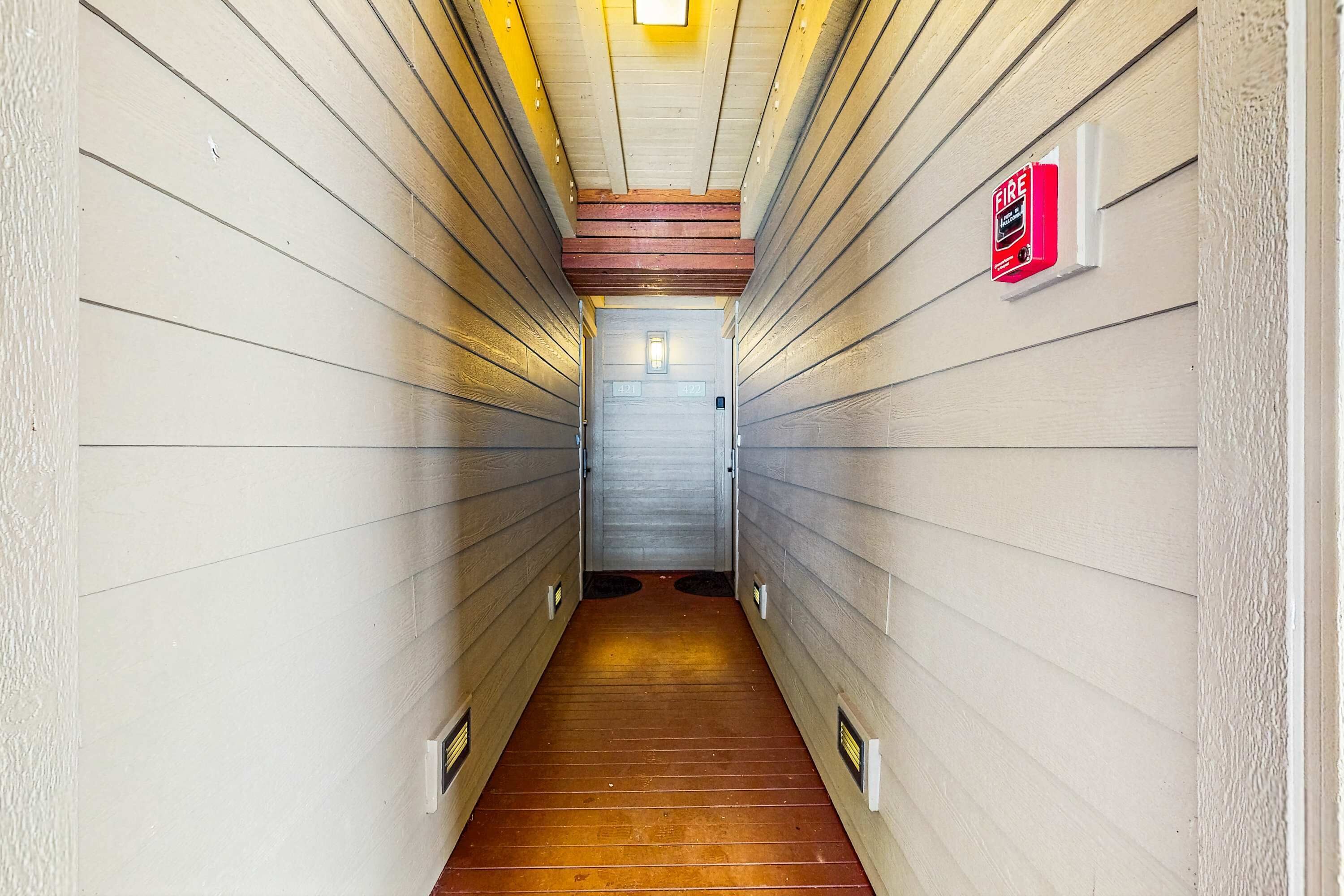 A narrow hallway with wooden flooring and white walls, leading to a door at the end.