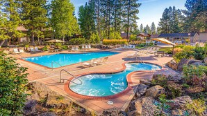 Une piscine dotée de chaises longues et d’un jacuzzi, entourée d’arbres et de rochers.