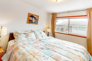 Une chambre à coucher comprenant un lit, une table de chevet, une lampe, une fenêtre avec des rideaux et un tableau accroché au mur.