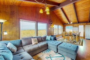 Un intérieur de chalet chaleureux avec un canapé d’angle, un pouf, une table à manger et des chaises.