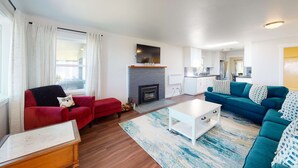 A living room with a fireplace, a red sofa, a teal sofa, and a white coffee table. - Beautifully renovated home across street from beach access - dogs welcome (Waldport)