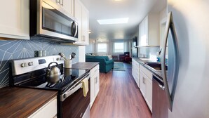A modern kitchen with a built-in oven, microwave, and kettle, a dining area with a red chair, and a view of the living room. - Beautifully renovated home across street from beach access - dogs welcome (Waldport)