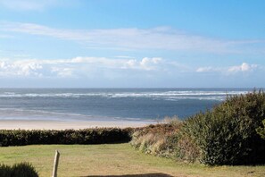 A coastal landscape with a beach, ocean, and a hedge in the foreground. - Beautifully renovated home across street from beach access - dogs welcome (Waldport)