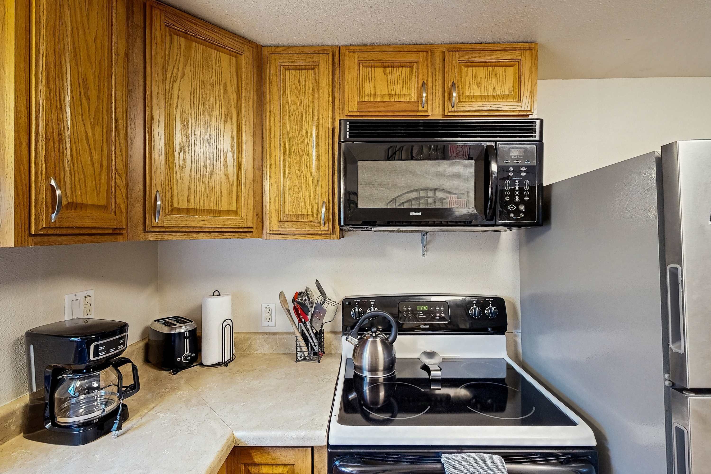 A kitchen with wooden cabinets, a microwave, a stove, a coffee maker, and a toaster.