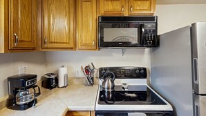 Una cocina con armarios de madera, microondas, estufa, cafetera y tostadora.