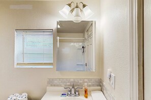 Ein Badezimmer mit einem weißen Waschbecken, einem Spiegel und einem Fenster mit Jalousien.