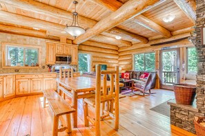 A log cabin interior with a wooden dining area, stone fireplace, and large windows. - Lodge with Two Decks & Great Location Close to Lake and Skiing (Government Camp)