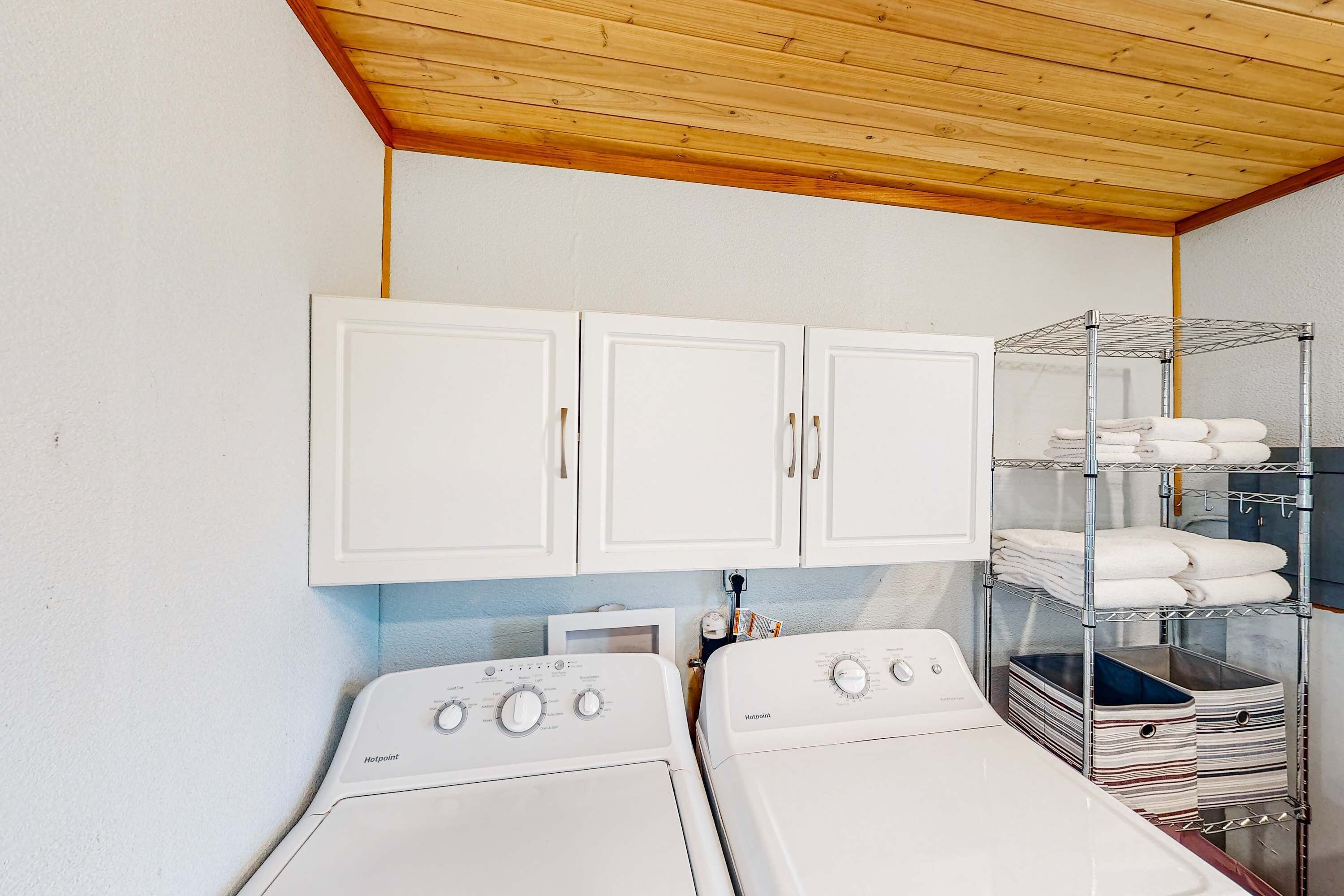A laundry room with two white front-loading washers, a metal drying rack, and a white cabinet above.