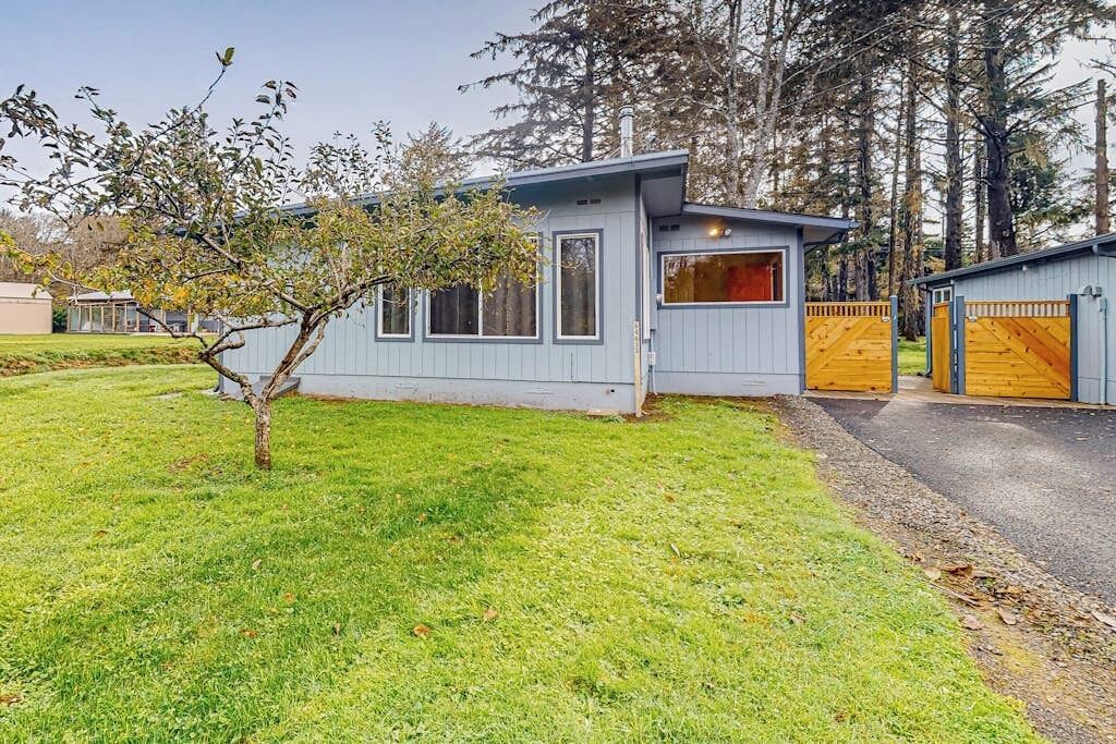 Une maison moderne de plain-pied avec un garage, une petite cour et un arbre.