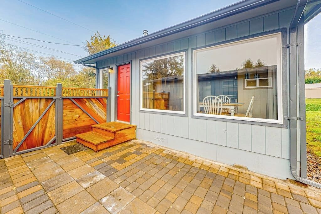 Un bâtiment avec une porte rouge, de grandes fenêtres et une clôture en bois.