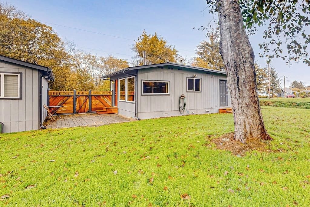 Une maison mobile de plain-pied avec un jardin clôturé, une terrasse en bois et un grand arbre.