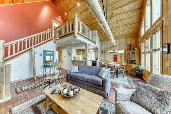 A spacious interior with a wooden staircase, a grey sofa, a wooden dining table, and a kitchen area.