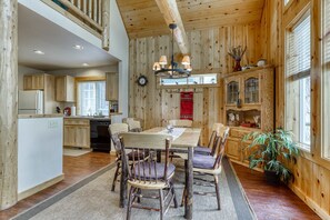 A wooden interior with a dining table, chairs, a kitchen area, and a clock on the wall.
