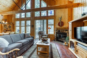 A log cabin interior with a fireplace, a television, a sofa, and a dining area.