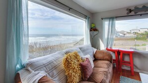 A room with a large window overlooking the beach, a sofa with cushions, and a red stool. - Ocean View Home with Free WiFi and Cable and a Full Kitchen - One Dog is Welcome (Newport)