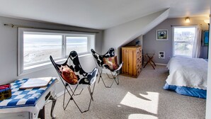 A bedroom with a bed, two chairs, a desk, a cabinet, and large windows. - Ocean View Home with Free WiFi and Cable and a Full Kitchen - One Dog is Welcome (Newport)