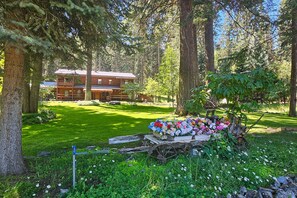 A wooden cabin surrounded by a lush garden with a cart of flowers. - Spacius family friendly home with a gas grill, full kitchen, W&D & wood stove (Joseph)