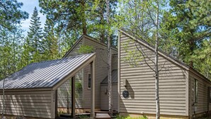 A rustic cabin with a sloped roof, a porch, and a chimney. - Home with hot tubs, pools, tennis, pickleball, gym, fireplace, & game room (Black Butte Ranch)
