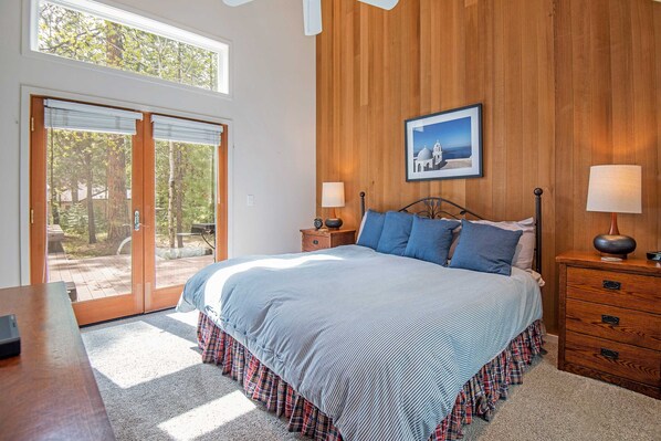 Un dormitorio con una cama grande, paredes de madera, un cuadro en la pared y vistas a través de la puerta de cristal.