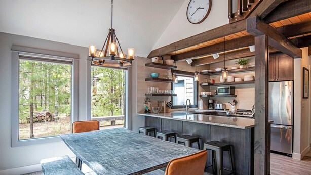 A modern kitchen with a large island, bar stools, and a dining table with benches. - Home with hot tubs, pools, tennis, pickleball, gym, fireplace, & game room (Black Butte Ranch)