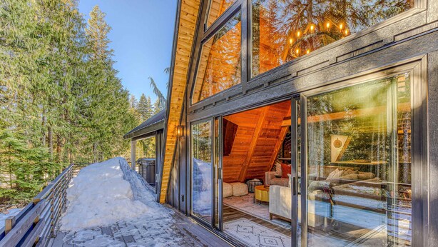 Ein modernes Blockhaus mit großen Fenstern, einer Holzterrasse und Blick auf einen Wald.