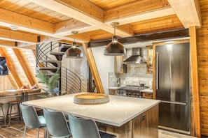 Une cuisine dotée d’un îlot central, un coin repas avec une table et des chaises, et un escalier menant à un niveau supérieur.
