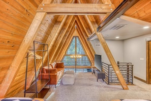 Une chambre mansardée avec un plafond en pente, une grande fenêtre, un canapé, un fauteuil et une petite table.