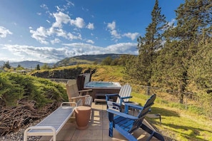 A hot tub with chairs and a table, surrounded by a fence, with a view of hills and trees.