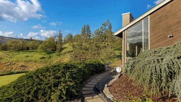 Une maison moderne avec un chemin de pierres menant à une porte en bois, entourée d’une végétation luxuriante et d’arbres.