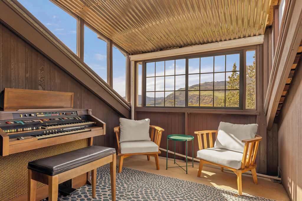 Une pièce avec un piano, deux chaises, une petite table et une vue sur l’extérieur.