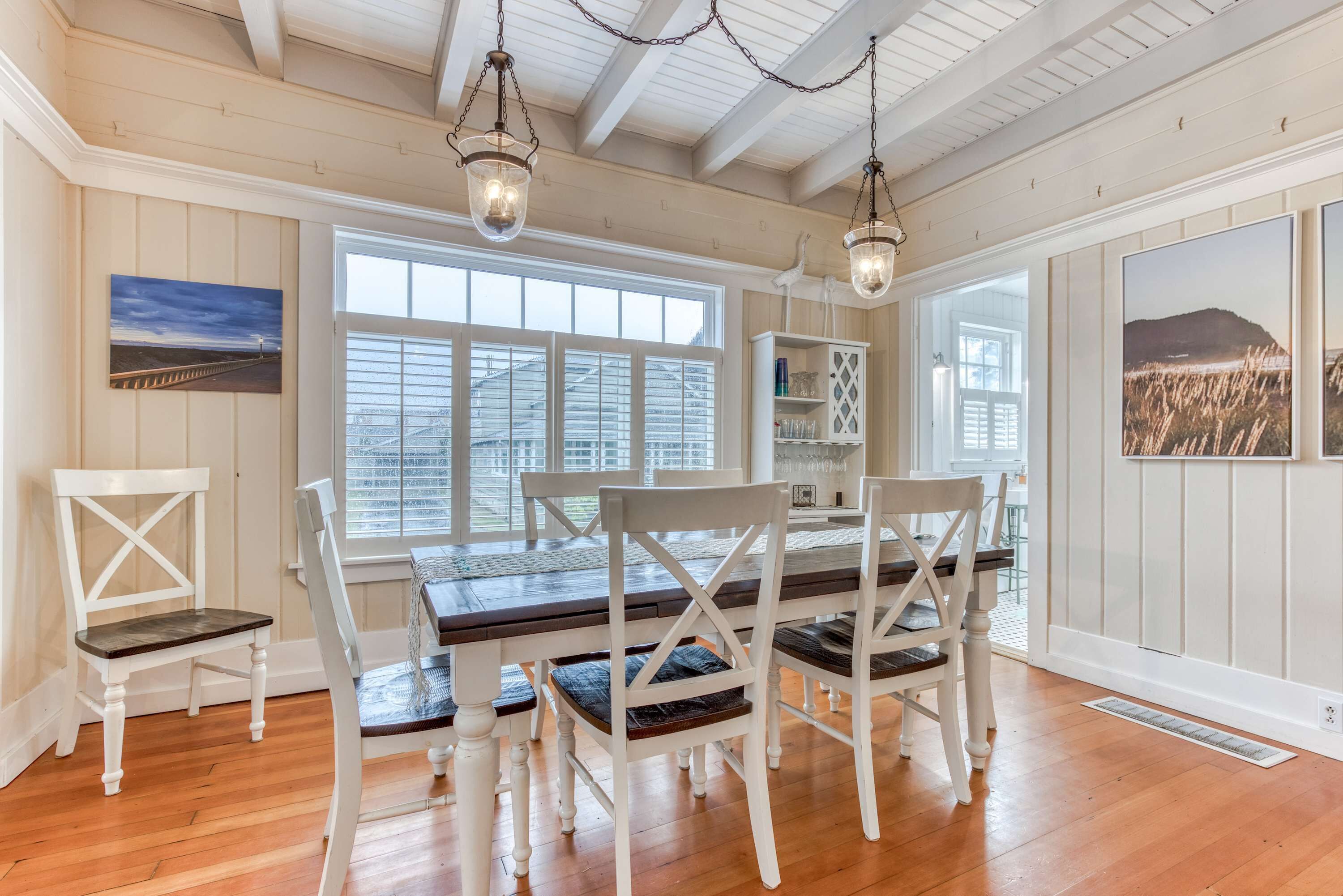 A dining area with a wooden table, white chairs, and pendant lights.