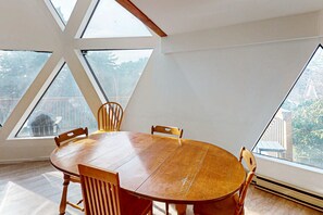 Een ronde houten tafel met stoelen in een kamer met grote, driehoekige ramen.