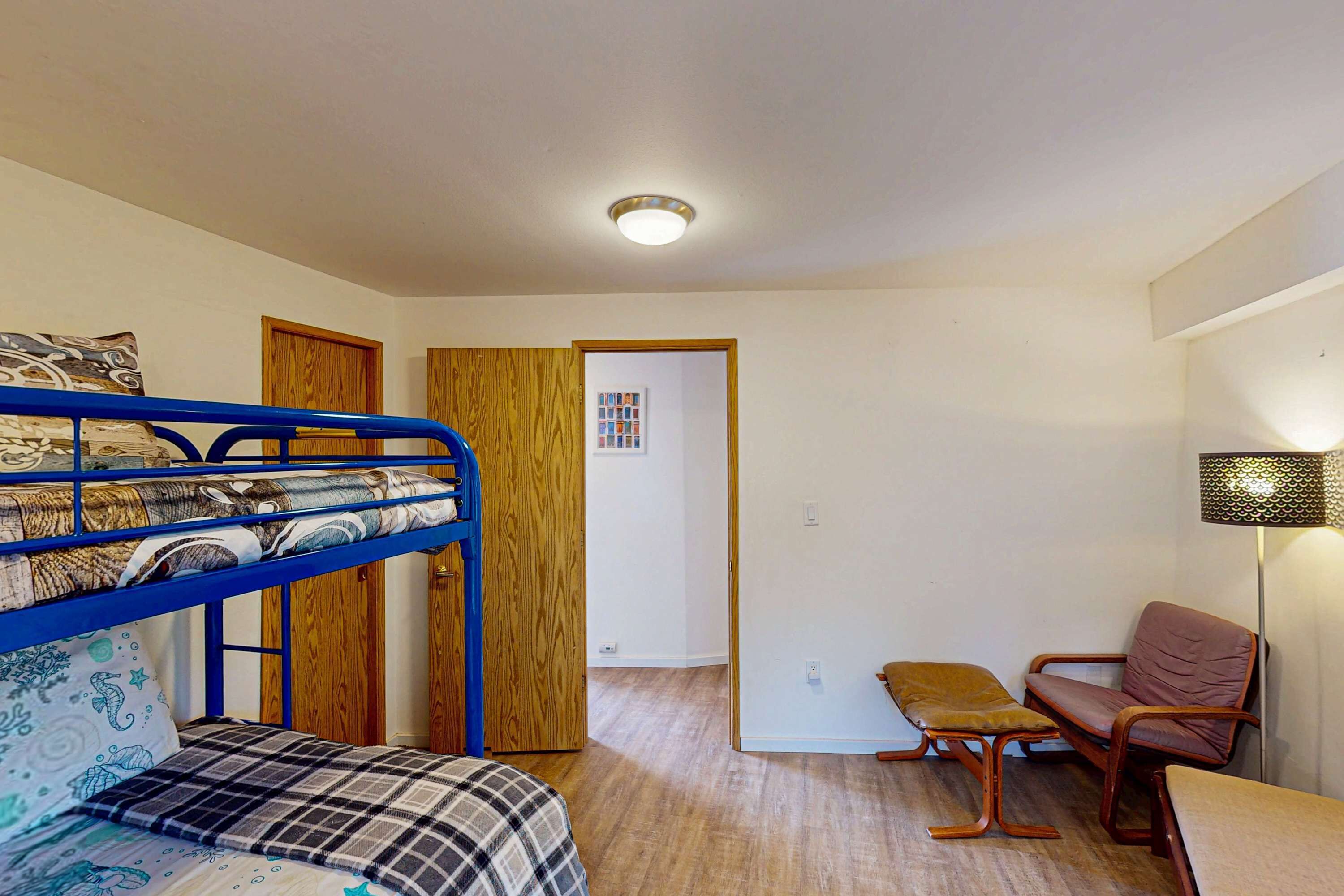 Ein Zimmer mit Etagenbetten, einer Holztür, einem kleinen Tisch, einem Stuhl und einer Lampe.