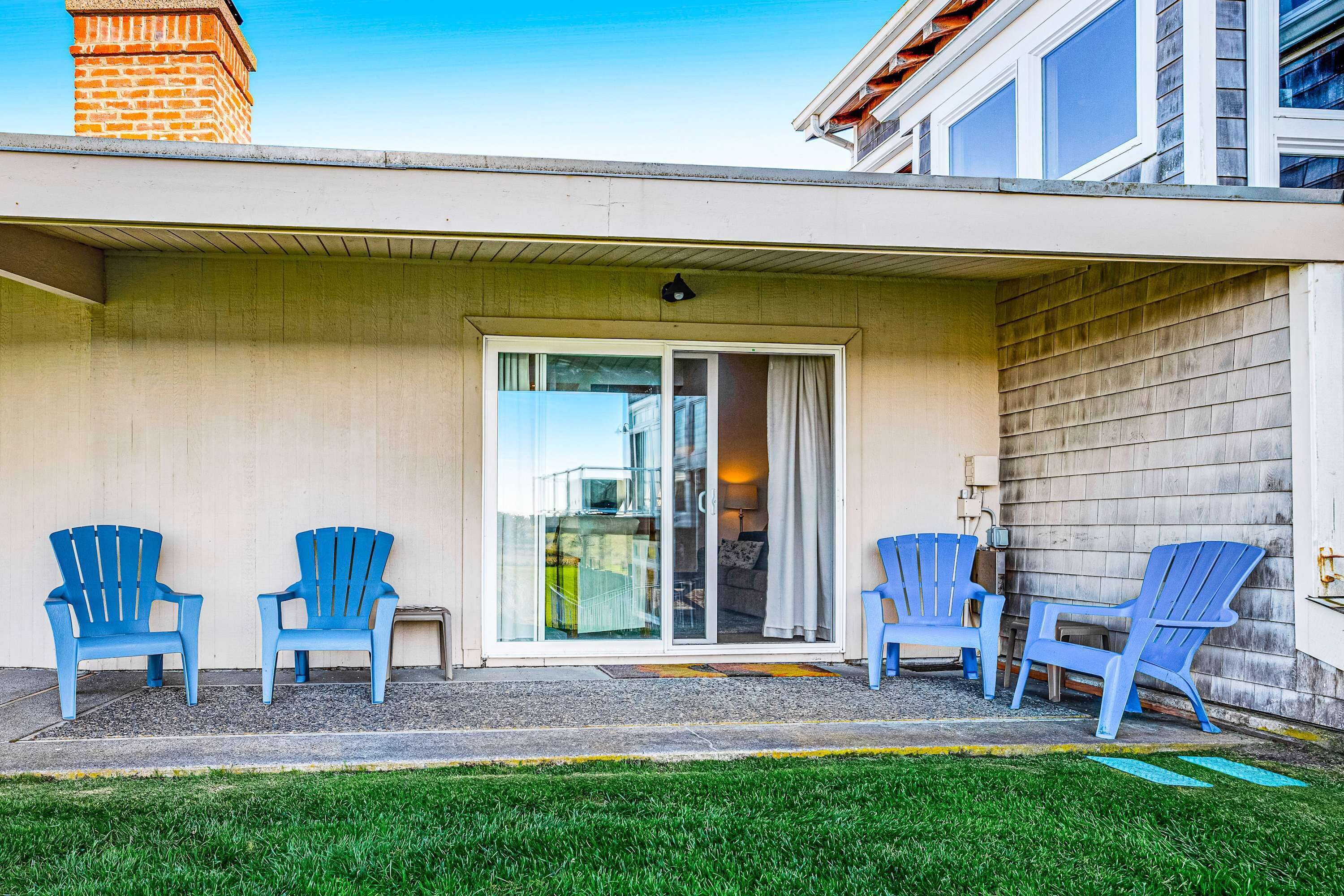A covered patio area with four blue chairs, a sliding glass door, and a brick chimney.