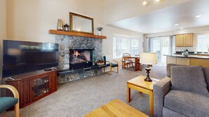 Un salón con chimenea de piedra, televisor de pantalla plana, sofá y comedor con mesa y sillas.