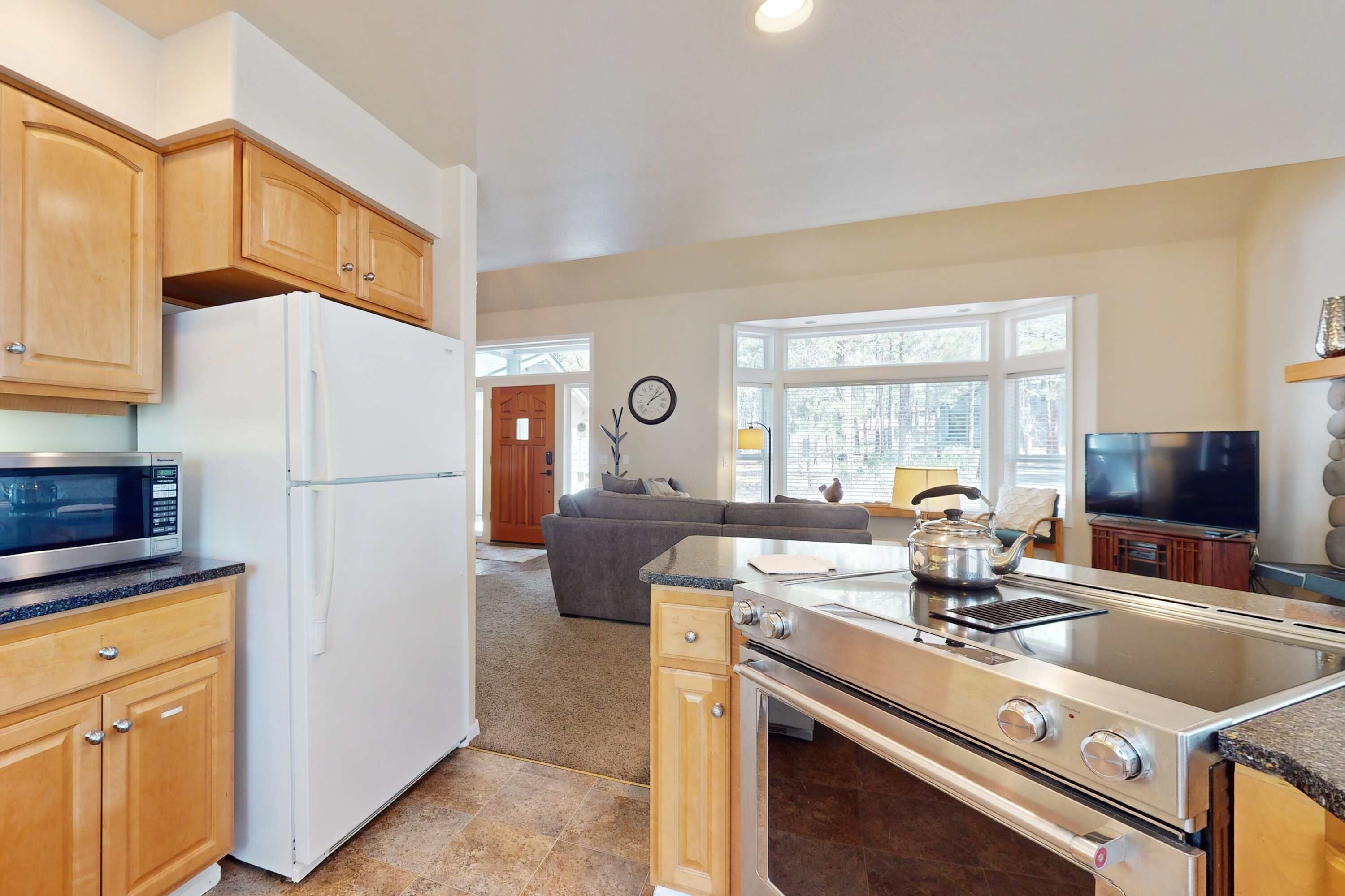 A modern kitchen with wooden cabinets, a white refrigerator, a microwave, a stove, and a large window.
