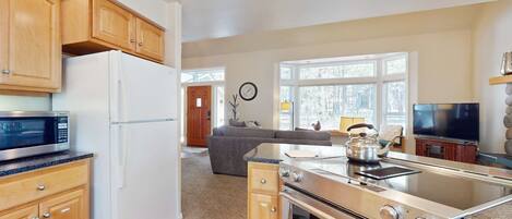 A modern kitchen with wooden cabinets, a white refrigerator, a microwave, a stove, and a large window.