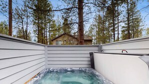 Un jacuzzi con cubierta de madera, rodeado de árboles y una casa al fondo.