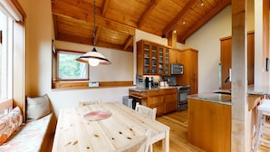 A wooden interior with a dining table, chairs, a kitchen area with cabinets, a microwave, and a hanging light fixture. - Tree-lined coastal home with wood fireplace, yard, W&D, & games - dog-friendly (Manzanita)