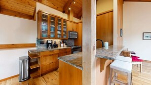 A kitchen with wooden cabinets, a microwave, a coffee maker, and a bar stool. - Tree-lined coastal home with wood fireplace, yard, W&D, & games - dog-friendly (Manzanita)