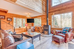 Un interior de cabaña con chimenea, muebles de cuero, paredes de madera y un televisor.