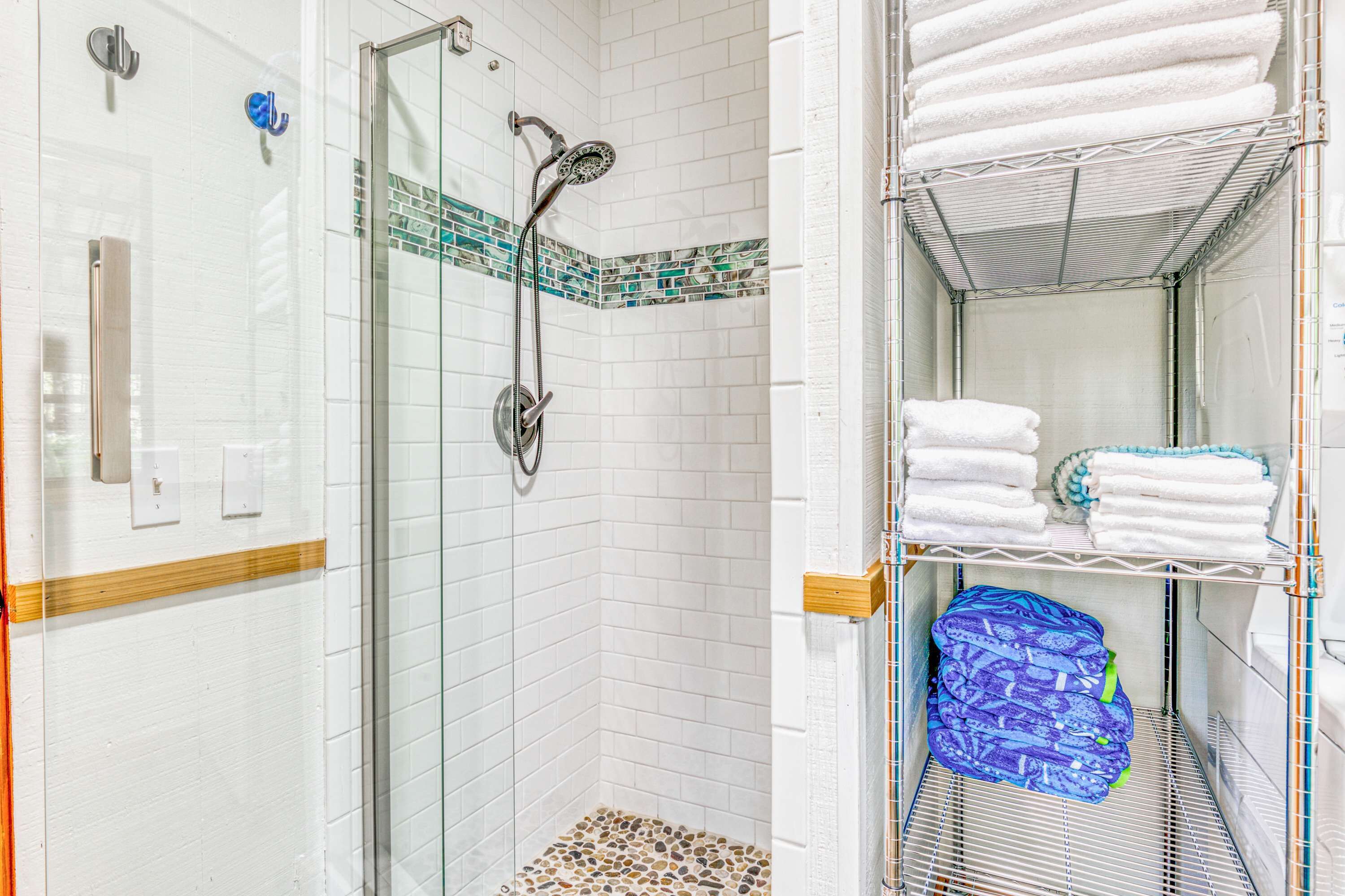 A shower with a glass door, a tiled floor, and a towel rack with folded towels.