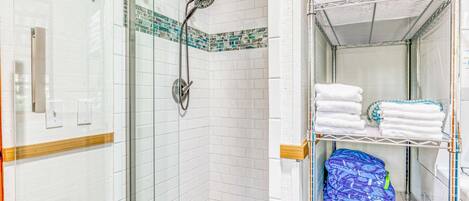 A shower with a glass door, a tiled floor, and a towel rack with folded towels.