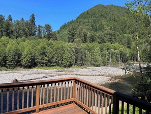 Une terrasse en bois donnant sur une rivière, avec une forêt dense en arrière-plan.