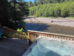 En træterrasse med jacuzzi med udsigt over en flod og skov.