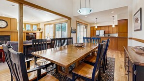Un comedor amplio con una larga mesa de madera y sillas, una cocina al fondo y un gran ventanal que proporciona luz natural.