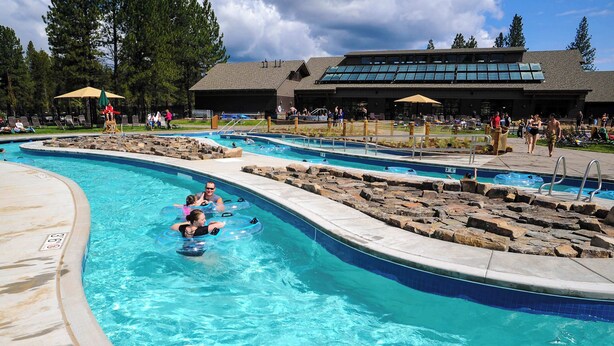 Una piscina con varias pistas, un puesto de socorrista y un edificio con un ventanal grande al fondo.