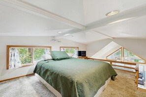 Une chambre avec un lit, une fenêtre, un ventilateur de plafond et une vue sur la verdure environnante.