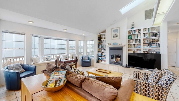A spacious living room with a large sofa, a coffee table, and a fireplace. There are bookshelves and a television. - Waterfront Family Home with Beach Access - Dog-friendly (Waldport)