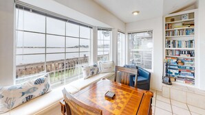 A room with a large window, a wooden table with a chessboard, a bookshelf, and a bench with cushions. - Waterfront Family Home with Beach Access - Dog-friendly (Waldport)